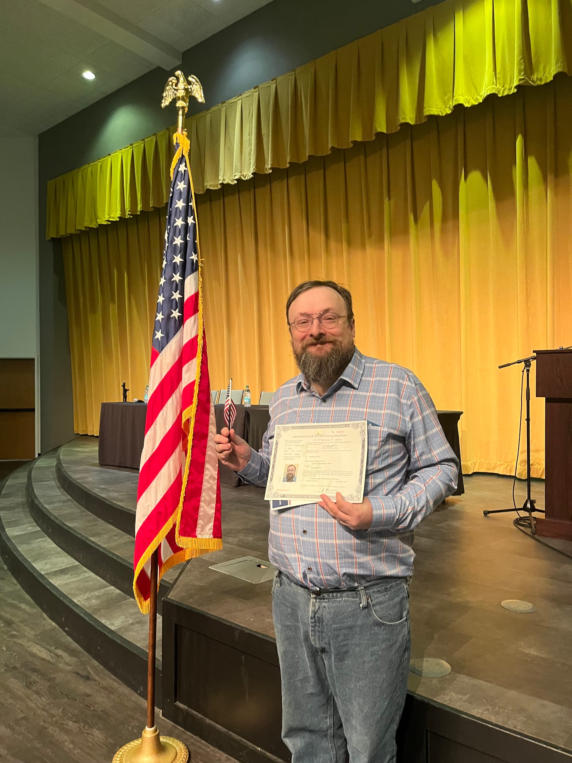 The author with a certificate and a little flag, standing next to a rather bigger flag.
